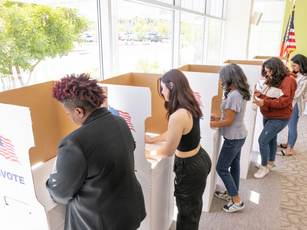 people lined up in voting booths voting with paper ballots