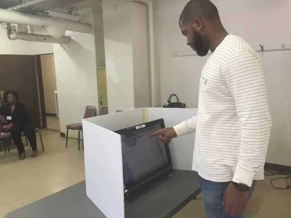 man using touchscreen voting machine at a voting booth